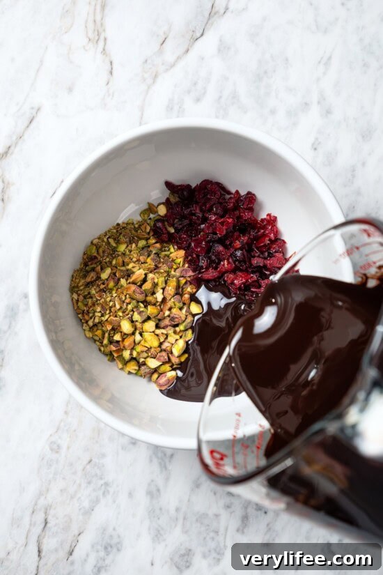 Dark Chocolate Bark with Pistachios and Cranberries Recipe 6 Pouring melted chocolate into bowl with pistachios and cranberries.