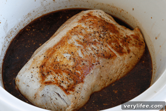 Boneless pork roast slow cooked in Asian spices creates an aromatic pork dish with mushrooms and broth, perfect over noodles or rice with fresh chopped green onions, cilantro and sriracha.