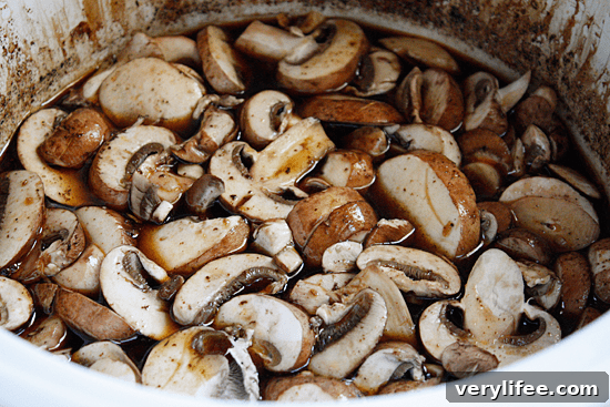Boneless pork roast slow cooked in Asian spices creates an aromatic pork dish with mushrooms and broth, perfect over noodles or rice with fresh chopped green onions, cilantro and sriracha.