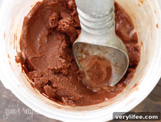 An ice cream scooper inside a bucket of chocolate sorbet.