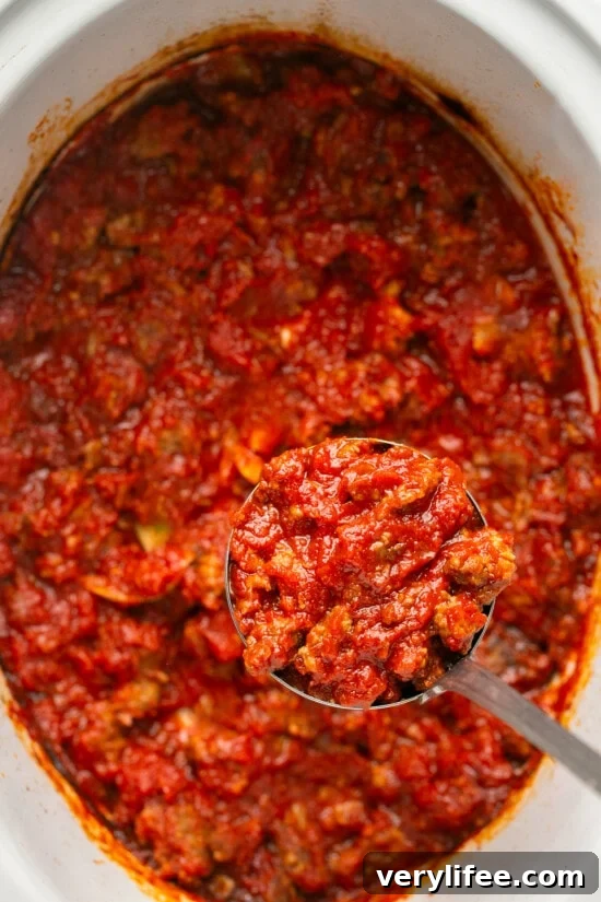 Crock Pot Sausage Pasta Sauce Recipe 7 A spoon lifting sausage pasta sauce from a crock pot.
