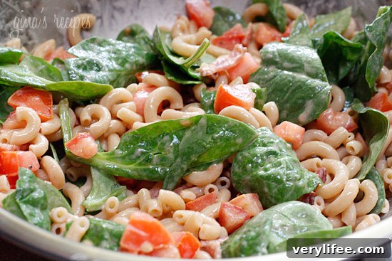 A bowl of elbow macaroni, baby spinach, and diced tomatoes coated with creamy dressing