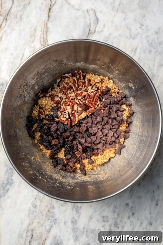 Homemade Chewy Pecan, Raisin and Chocolate Chip Granola Bars 8 Raisins, chocolate chips, and pecans added to granola bar mixture in bowl.