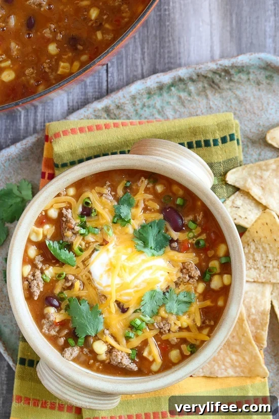 Hearty Taco Soup Recipe with Ground Beef and Beans 2 Overhead view of a bowl of turkey taco soup with sour cream, cheese, and cilantro.