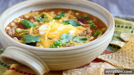 Hearty Taco Soup Recipe with Ground Beef and Beans 3 Side view of a bowl of turkey taco soup with sour cream, shredded cheddar cheese, and cilantro.