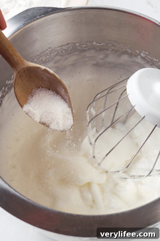 Add sugar gradually to the whipped egg whites Spooning sugar into bowl of whipped egg whites