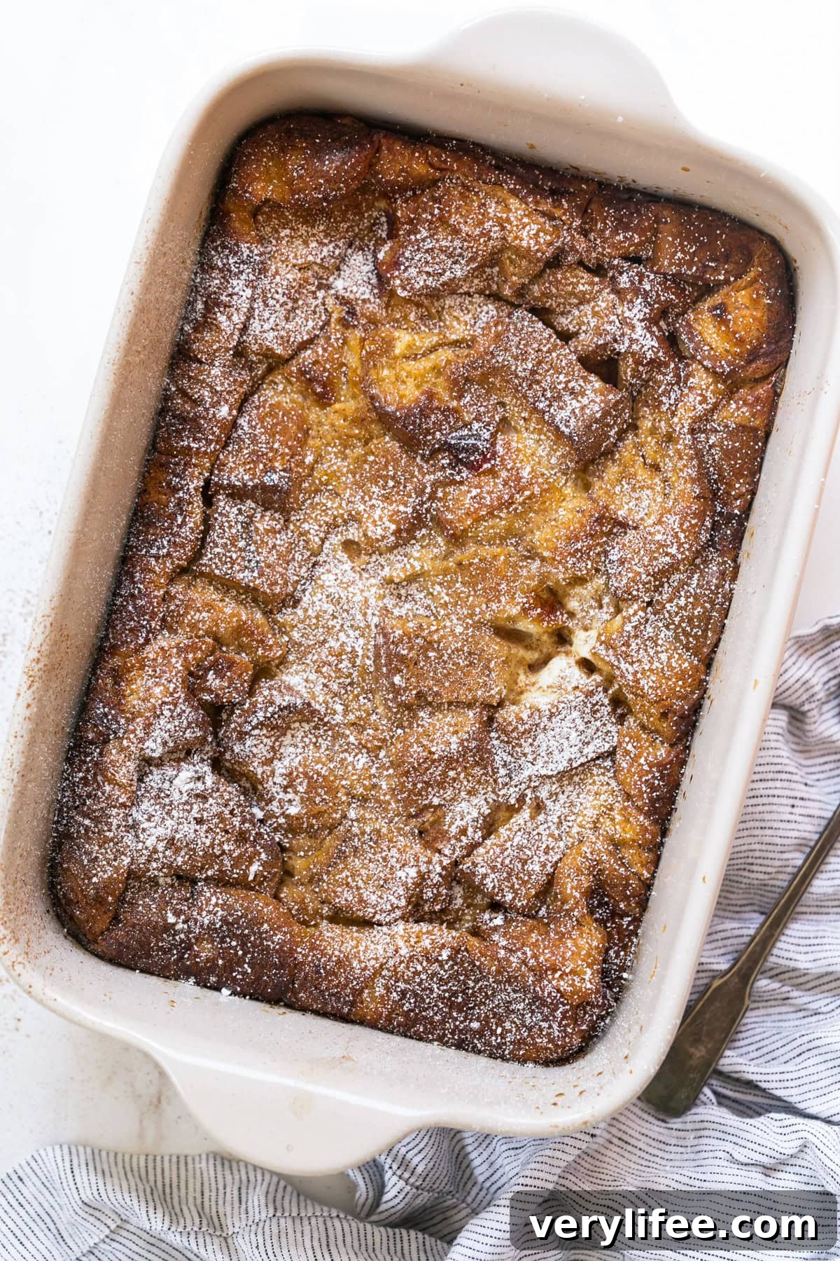 Overhead view of a baked creme brulee French toast casserole dusted with powdered sugar.