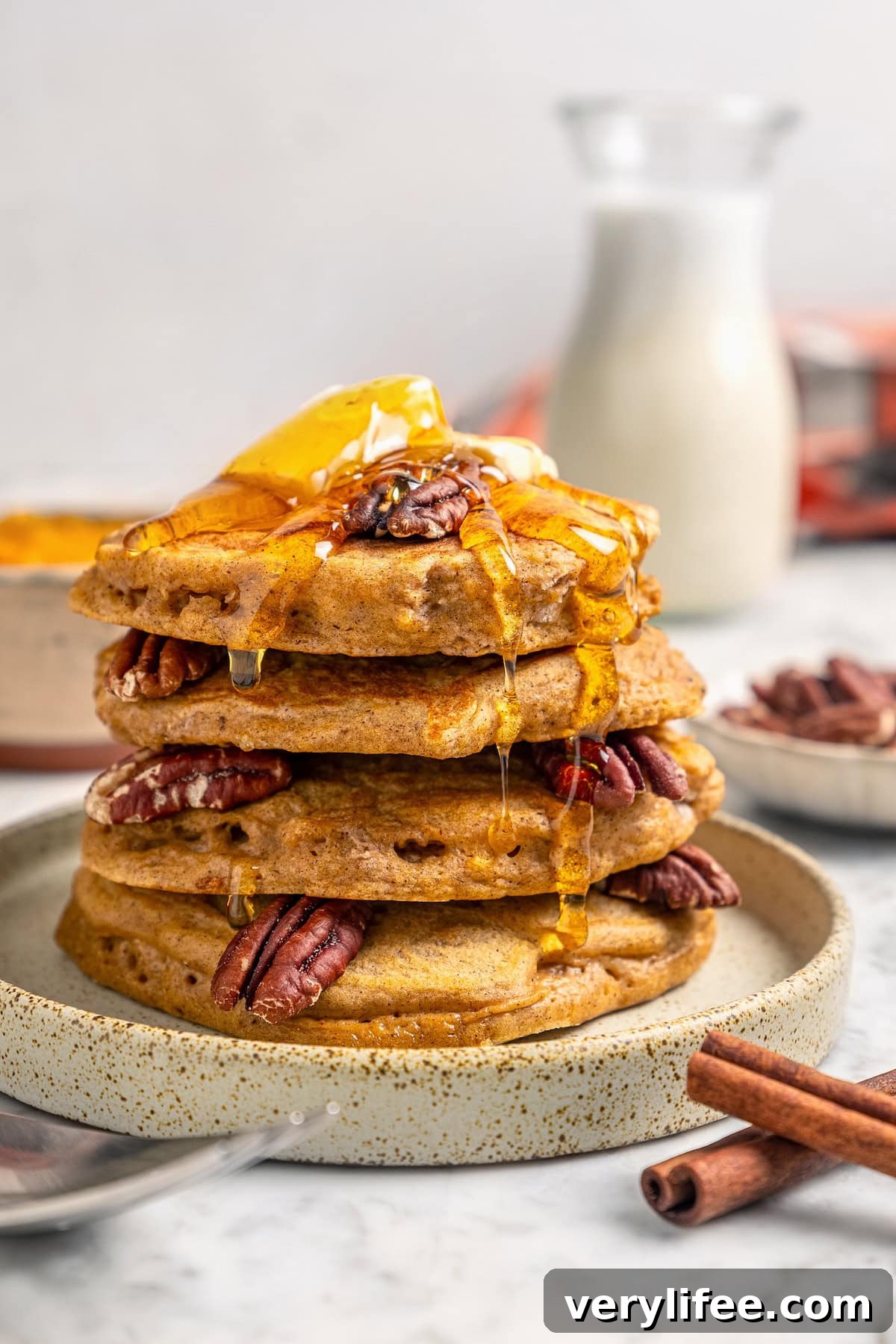 Stack of pumpkin pancakes on plate with syrup, pecans, and butter
