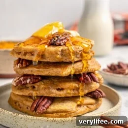 Stack of pumpkin pancakes on plate with syrup, pecans, and butter
