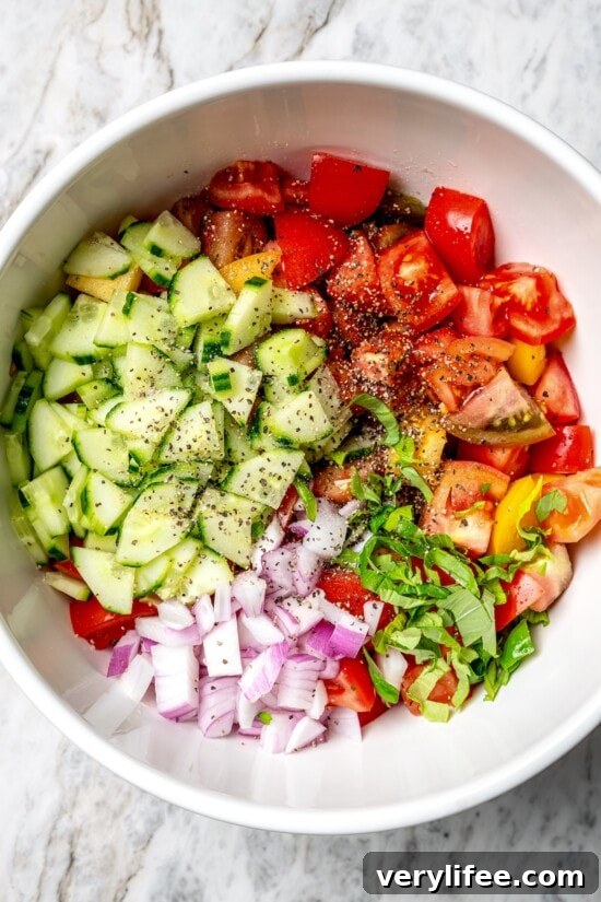 Overhead view of basil, tomatoes, red onions, and cucumbers in bowl for panzanella