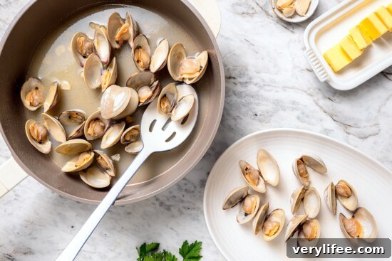 Tender Steamed Clams with Garlic and White Wine 9 Slotted spoon removing steamed clams from skillet.