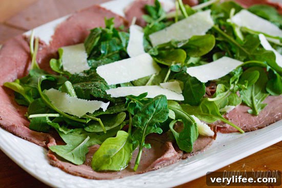 Classic Beef Carpaccio Recipe with Arugula and Parmesan 2 A platter with thin sliced roast beef, arugula and shaved asiago