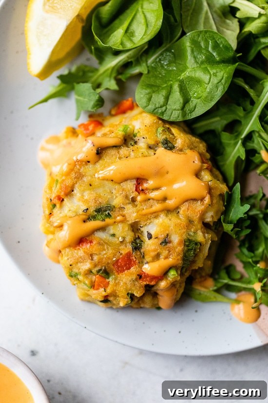Baked Lump Crab Cakes with Red Pepper Sauce A baked lump crab cake drizzled with red pepper sauce next to a green salad on a plate.