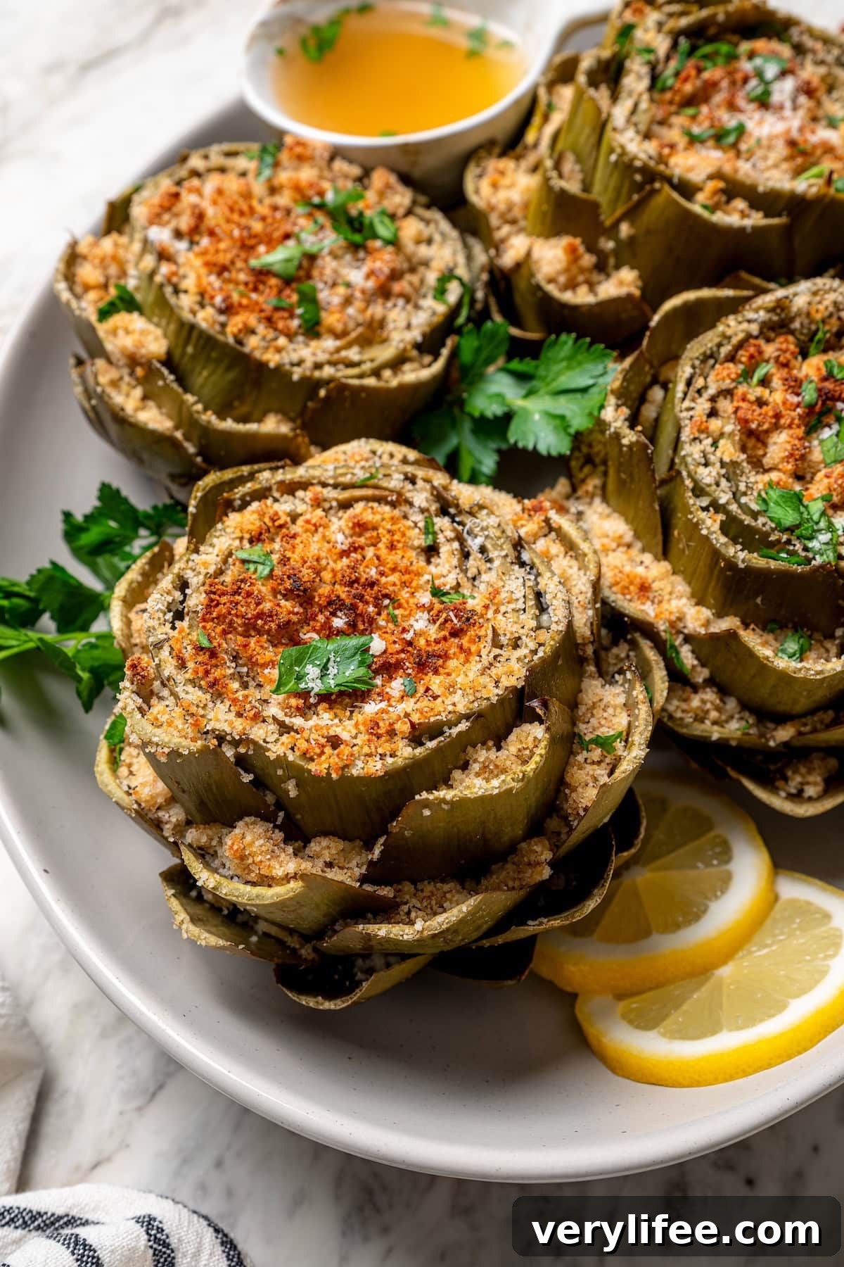 Stuffed artichokes are a classic Italian dish made with crispy, cheesy breadcrumbs. My version is a bit lighter but just as delicious! Platter of stuffed artichokes with sliced lemon