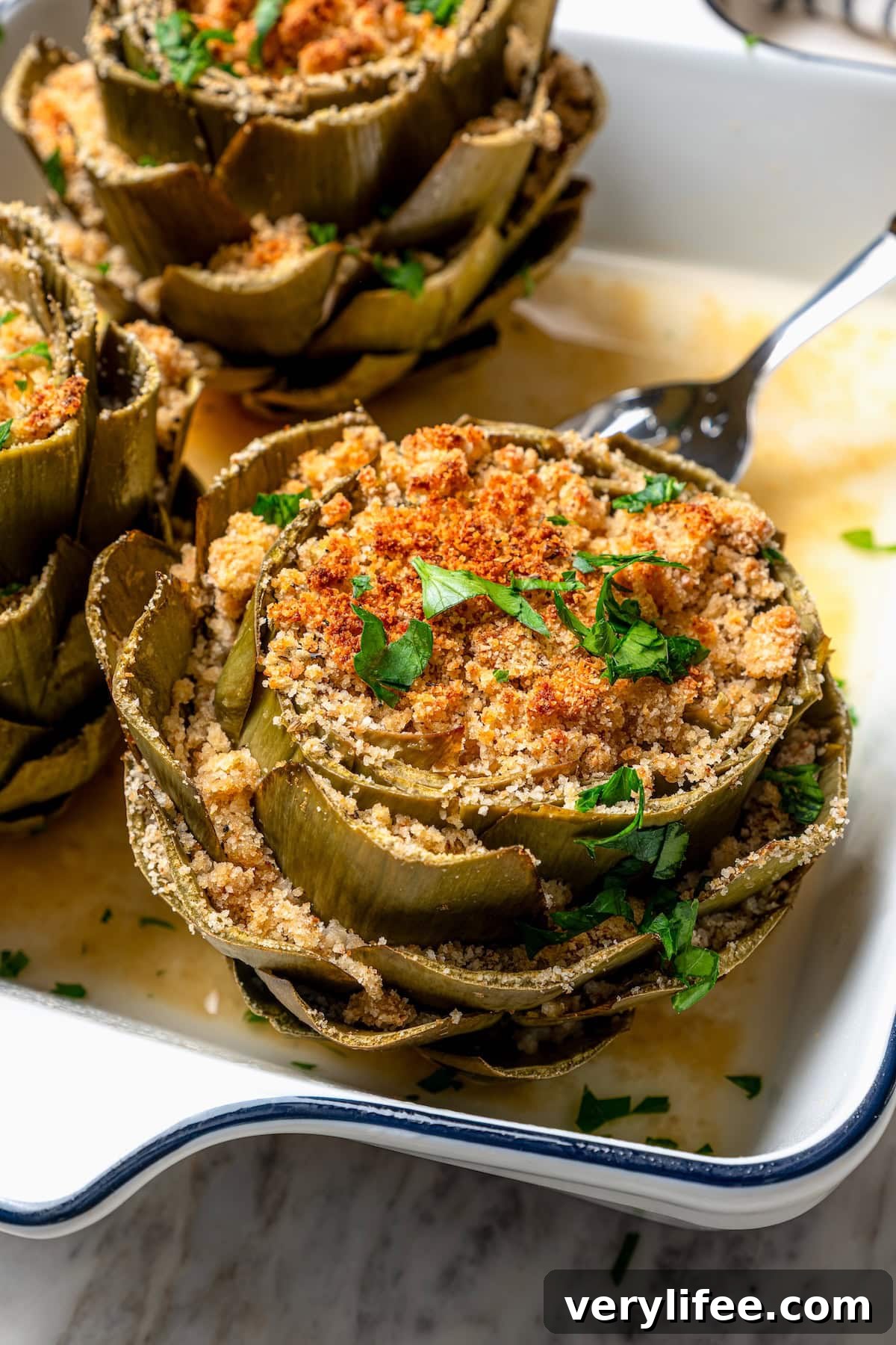Garlic-Parmesan Stuffed Artichokes Recipe 8 Fork lifting stuffed artichoke from baking dish