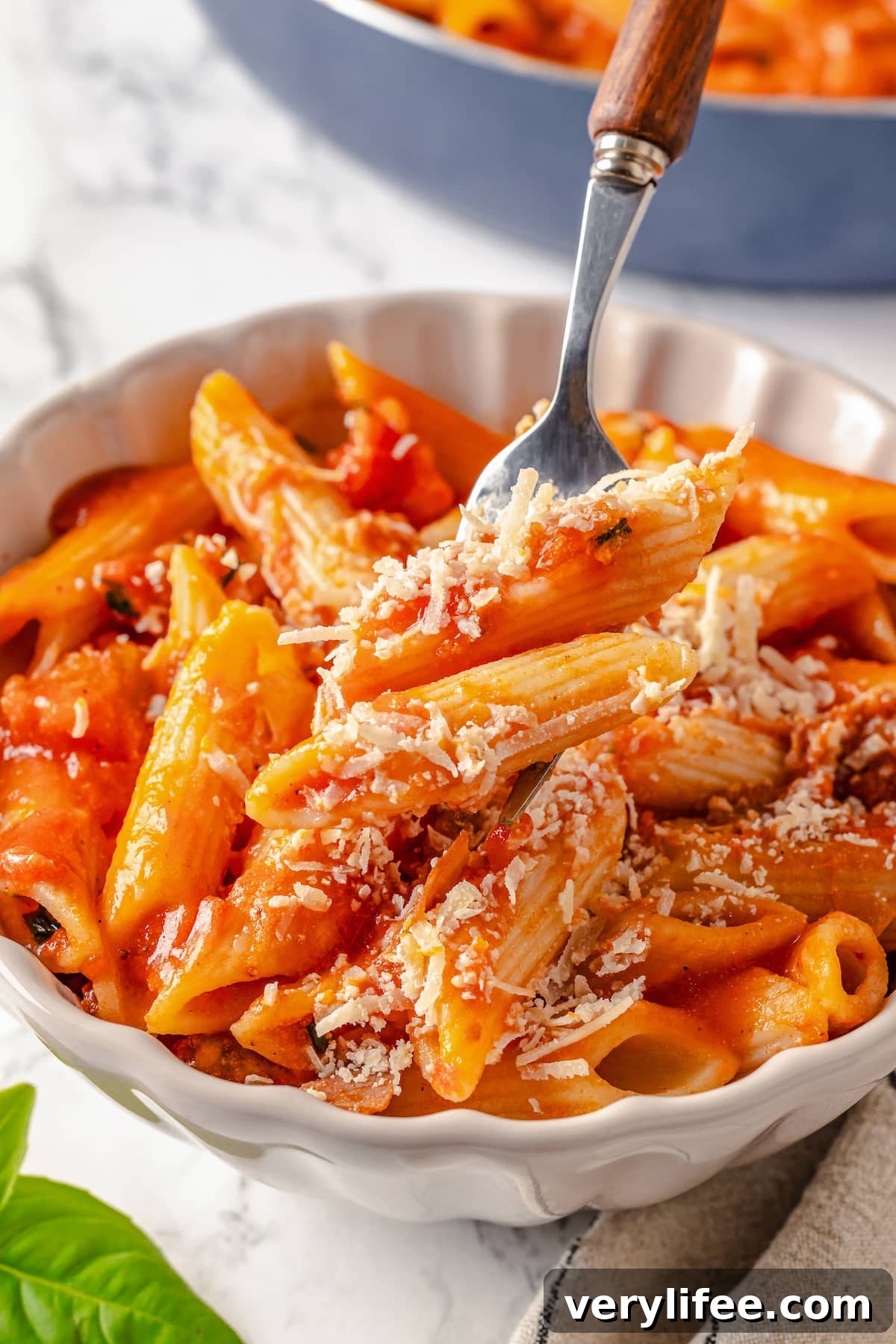 A fork showing a bite of penne alla vodka over a bowl