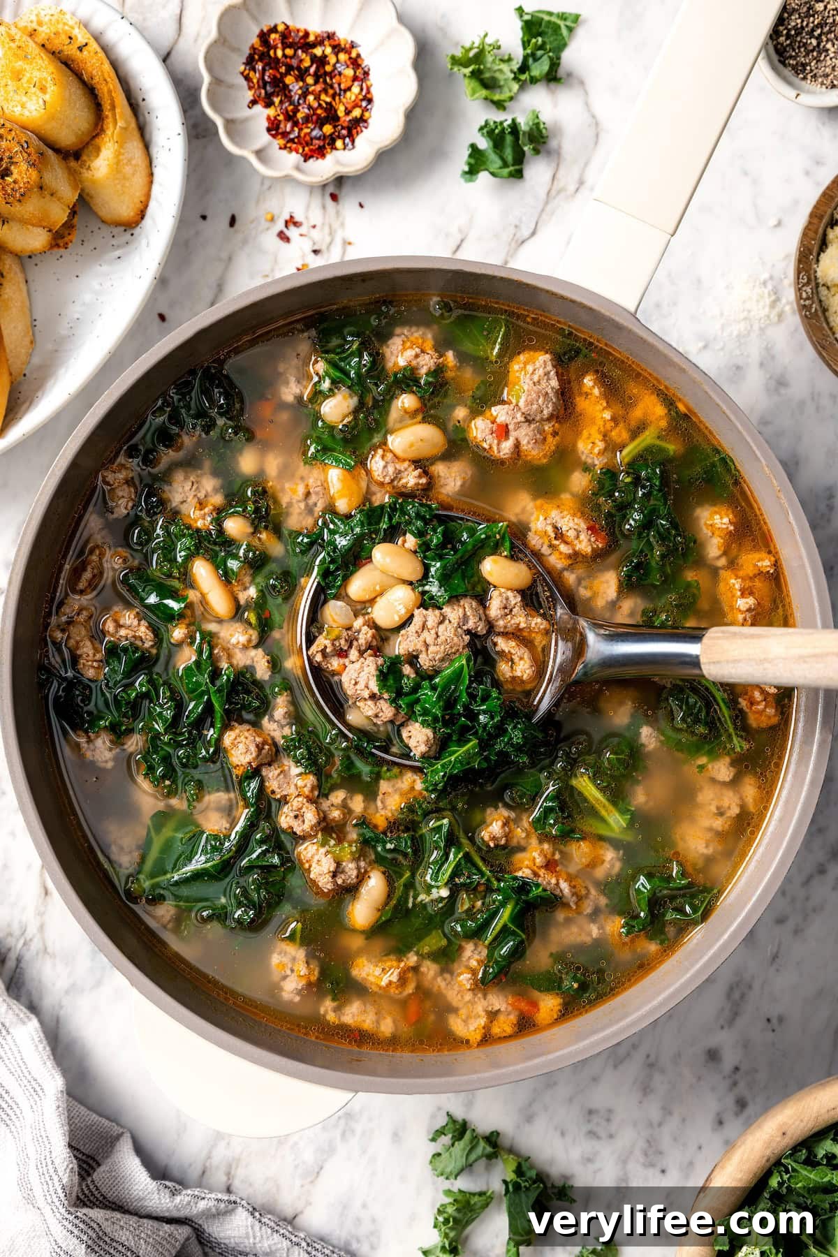 Ladle in pot of white bean soup with sausage and kale.