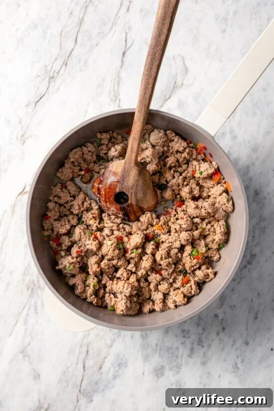 Browning turkey sausage in skillet with wooden spoon.