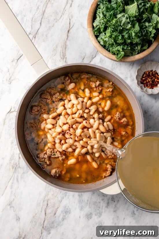 Pouring chicken stock into pot of white bean soup.