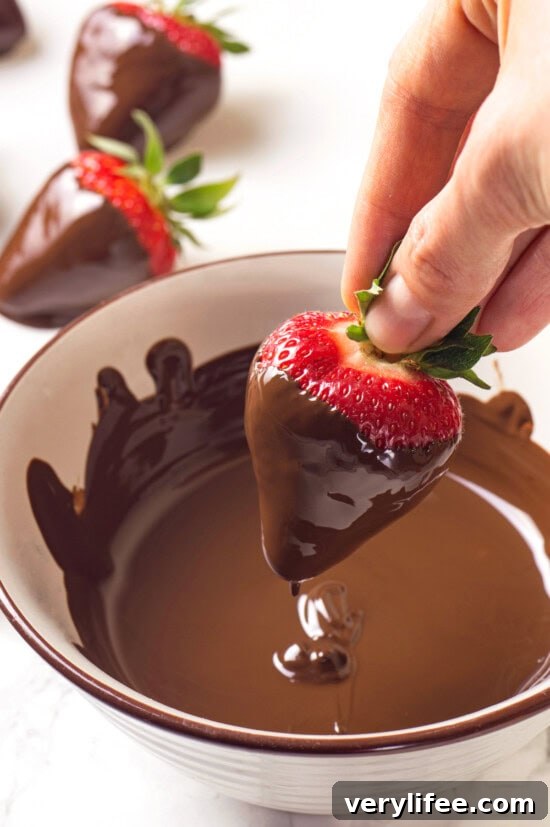 Dip the strawberries Hand dipping strawberry into bowl of melted chocolate