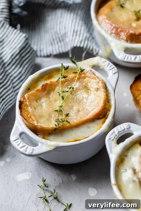 French onion soup in ramekins topped with toast and melted cheese, garnished with thyme sprigs.