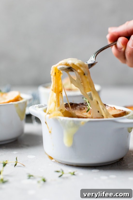 A spoonful of cheesy French onion soup being lifted from a ramekin.