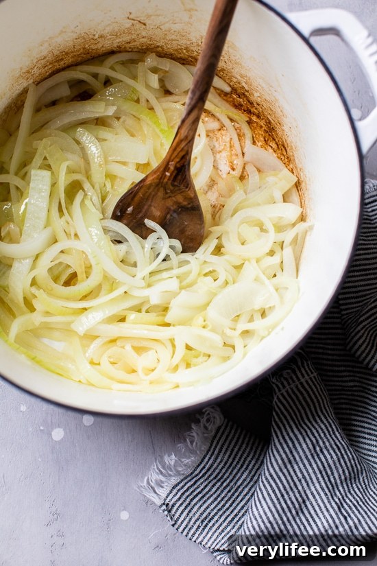 Sliced onions being stirred in a pot by a wooden spoon.