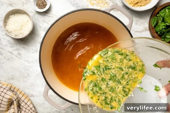 Classic Italian Stracciatella Soup with Spinach and Orzo 6 Pouring egg mixture into pot of broth.