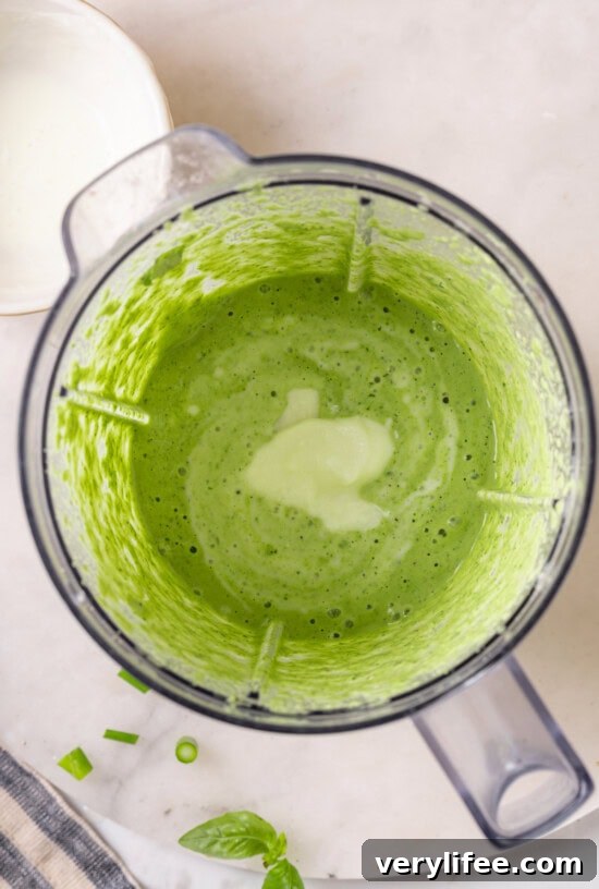 Overhead view of sour cream added to blender of basil green goddess dressing