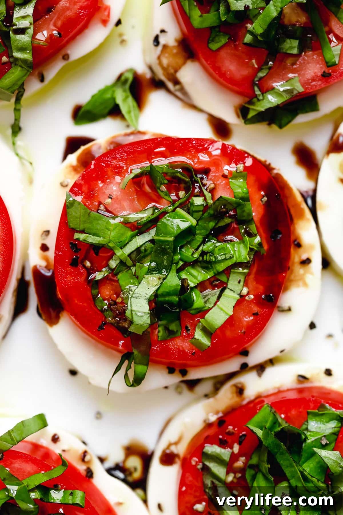 Caprese salad is a simple summer salad with fresh mozzarella, thick slices of juicy tomatoes, basil and a splash of balsamic vinegar. So easy! Overhead closeup of Caprese salad on platter