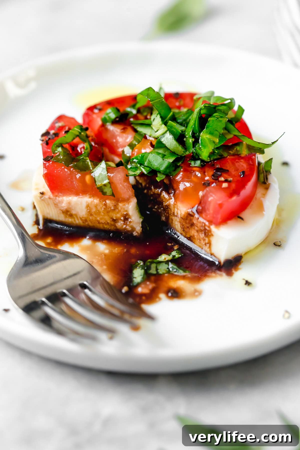 Caprese salad is a simple summer salad with fresh mozzarella, thick slices of juicy tomatoes, basil and a splash of balsamic vinegar. So easy! Caprese salad on plate with fork