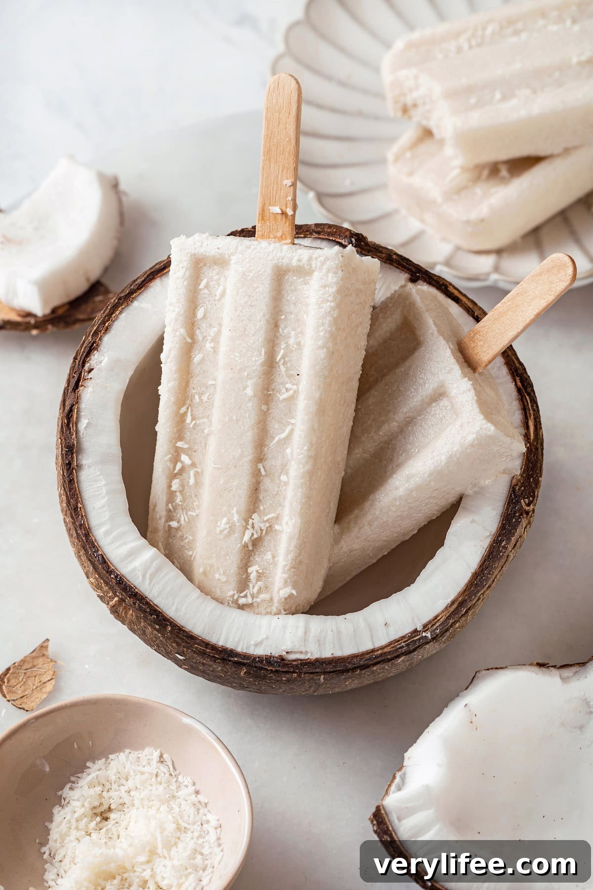 These homemade coconut popsicles are rich, creamy, and super simple to make. Two coconut popsicles set in halved coconut