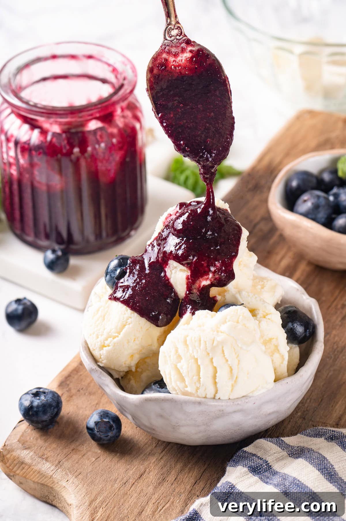 Spoon compote over ice cream for a quick dessert. Spooning blueberry fruit compote onto bowl of vanilla ice cream
