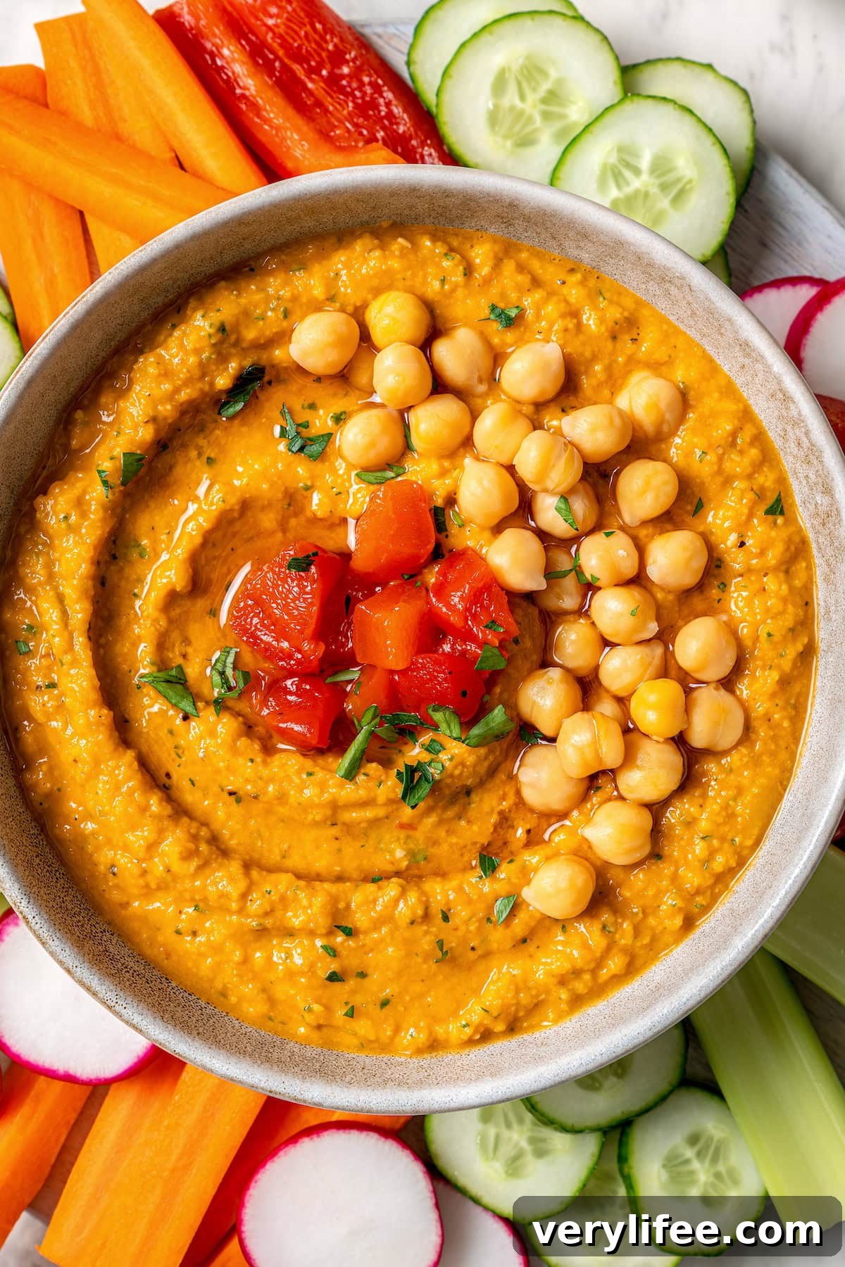 Overhead view of roasted red pepper hummus in bowl surrounded by fresh veggies