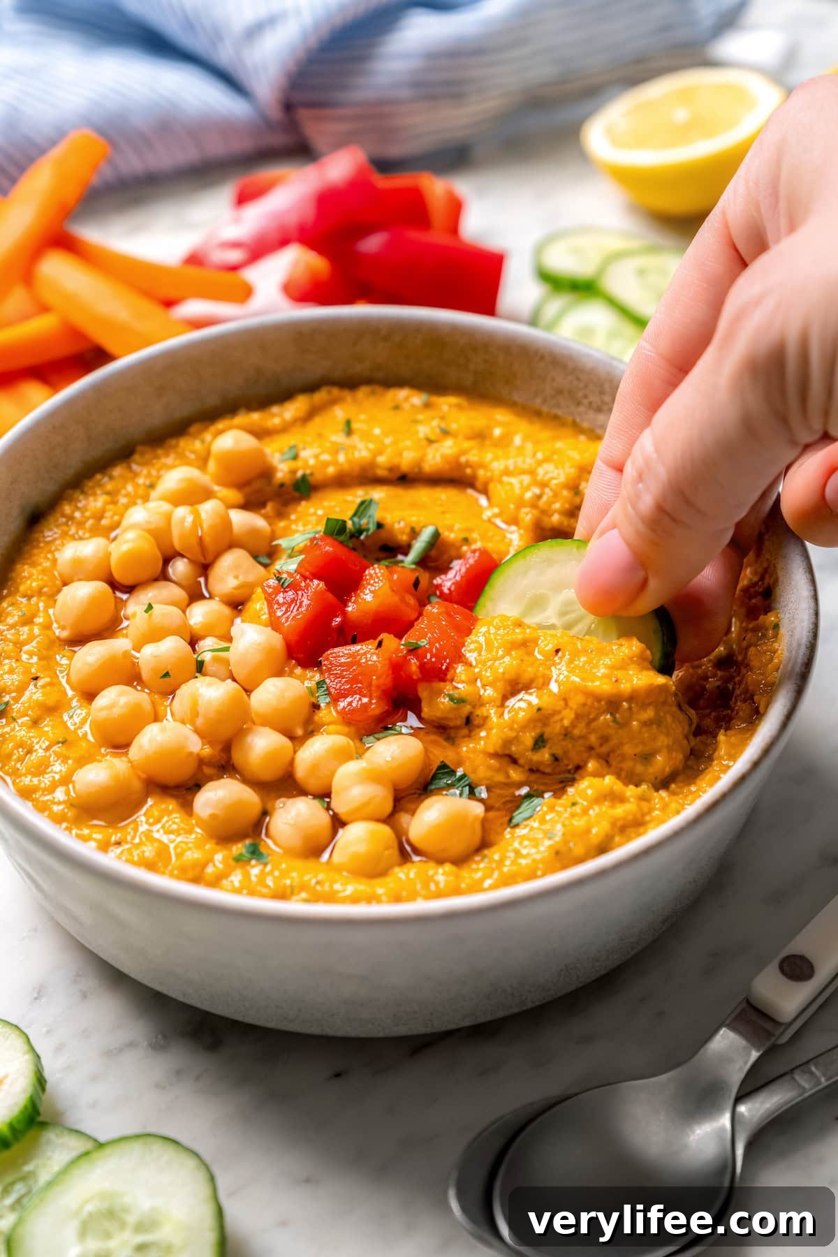 Dipping cucumber into roasted red pepper hummus