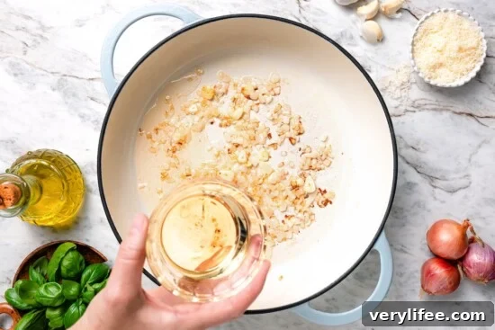Creamy Basil Mussels Recipe 6 Hand holding wine above skillet with aromatics.