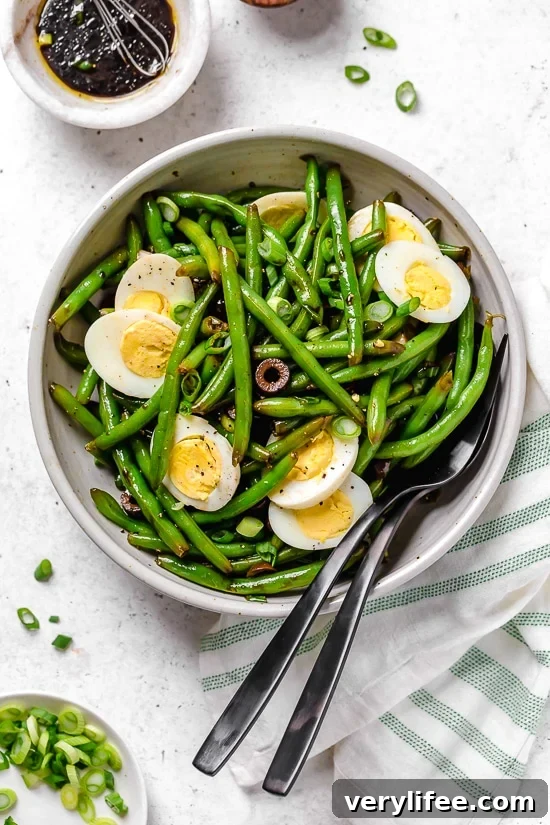 Bowl of green bean salad with hard-boiled eggs, olives, and scallions.