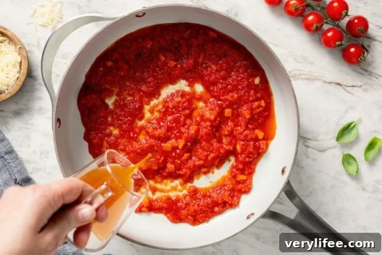 Pouring broth into skillet of sauce.