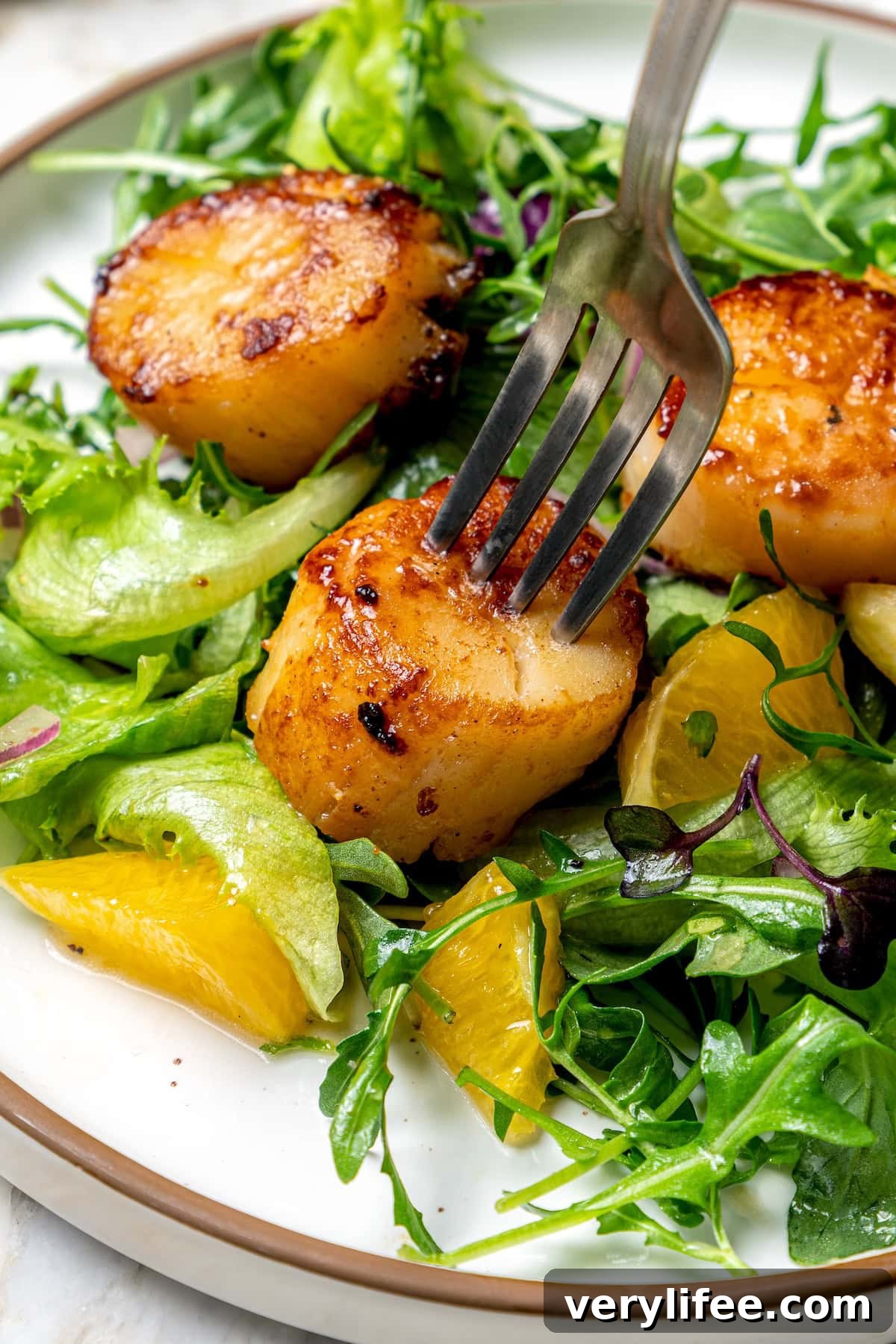Fork piercing pan seared scallop on plate with salad