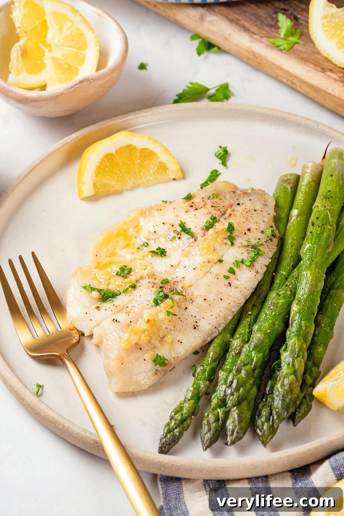 This simple baked tilapia recipe is finished with a garlicky lemon butter sauce and parsley, making it a delicious and light weeknight dinner! Easy baked tilapia on plate with asparagus
