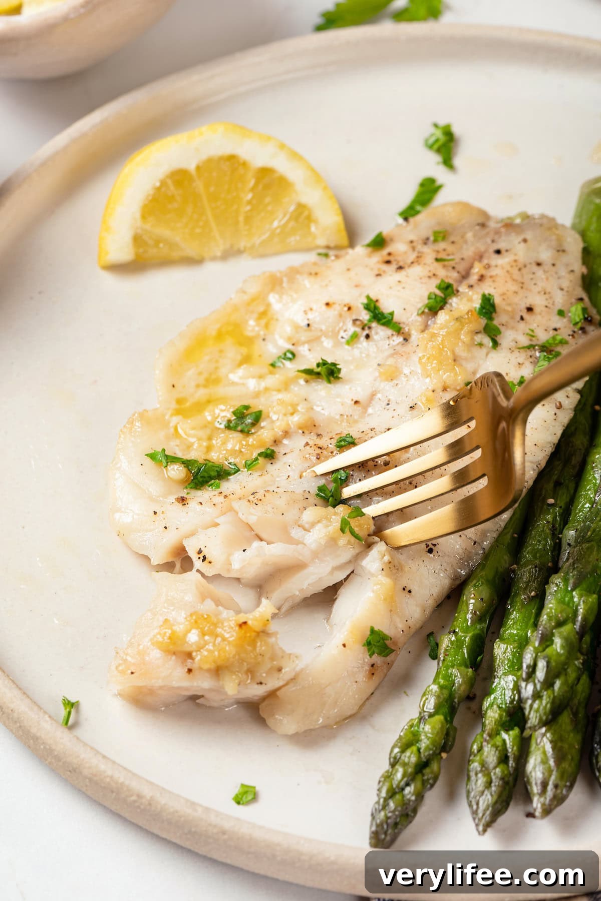 Crispy Oven Baked Tilapia with Lemon and Herbs 8 Fork cutting into baked tilapia on plate with asparagus