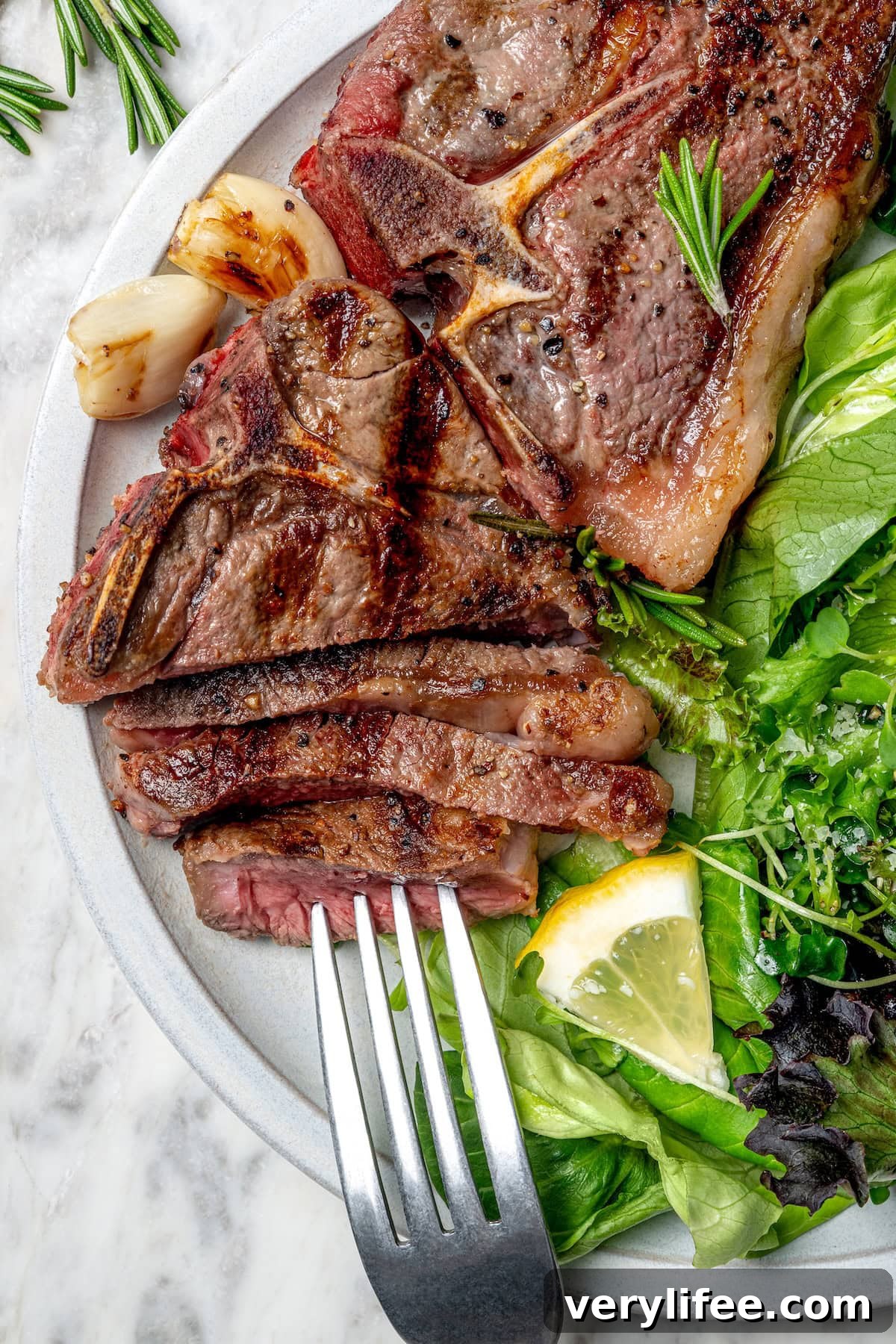 Grilled Rosemary Lamb Chops Recipe with Garlic and Lemon 11 Sliced grilled lamb chop on plate with salad and fork