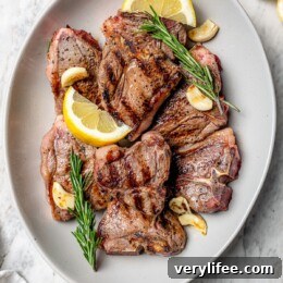 Overhead view of grilled lamb chops on platter with fresh rosemary, lemon wedges, and garlic cloves