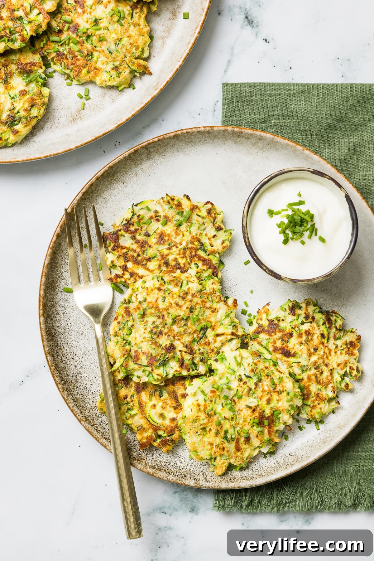 Overhead view of crispy zucchini pancakes next to dipping sauce on a plate.