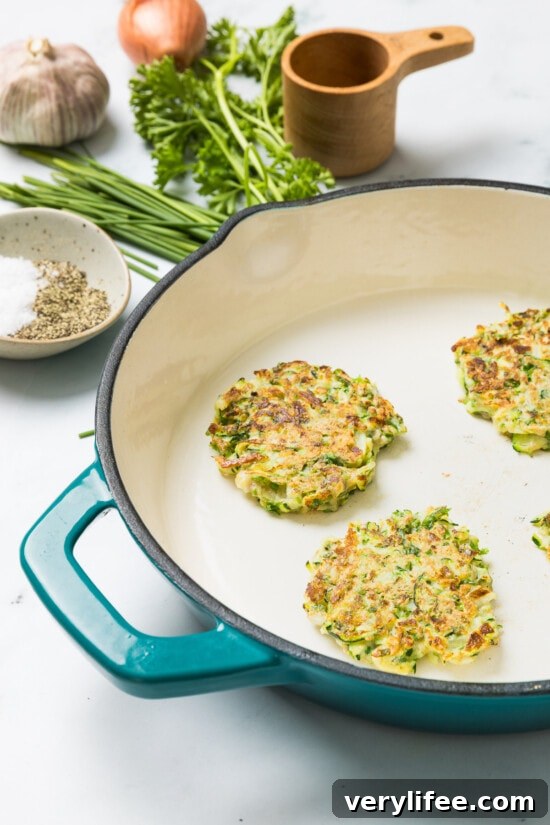 Zucchini pancakes cooking in a skillet.