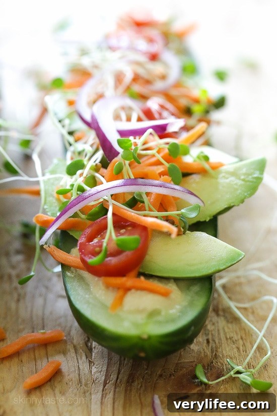 Close-up of a cucumber half scooped and filled with hummus, avocado and sprouts.