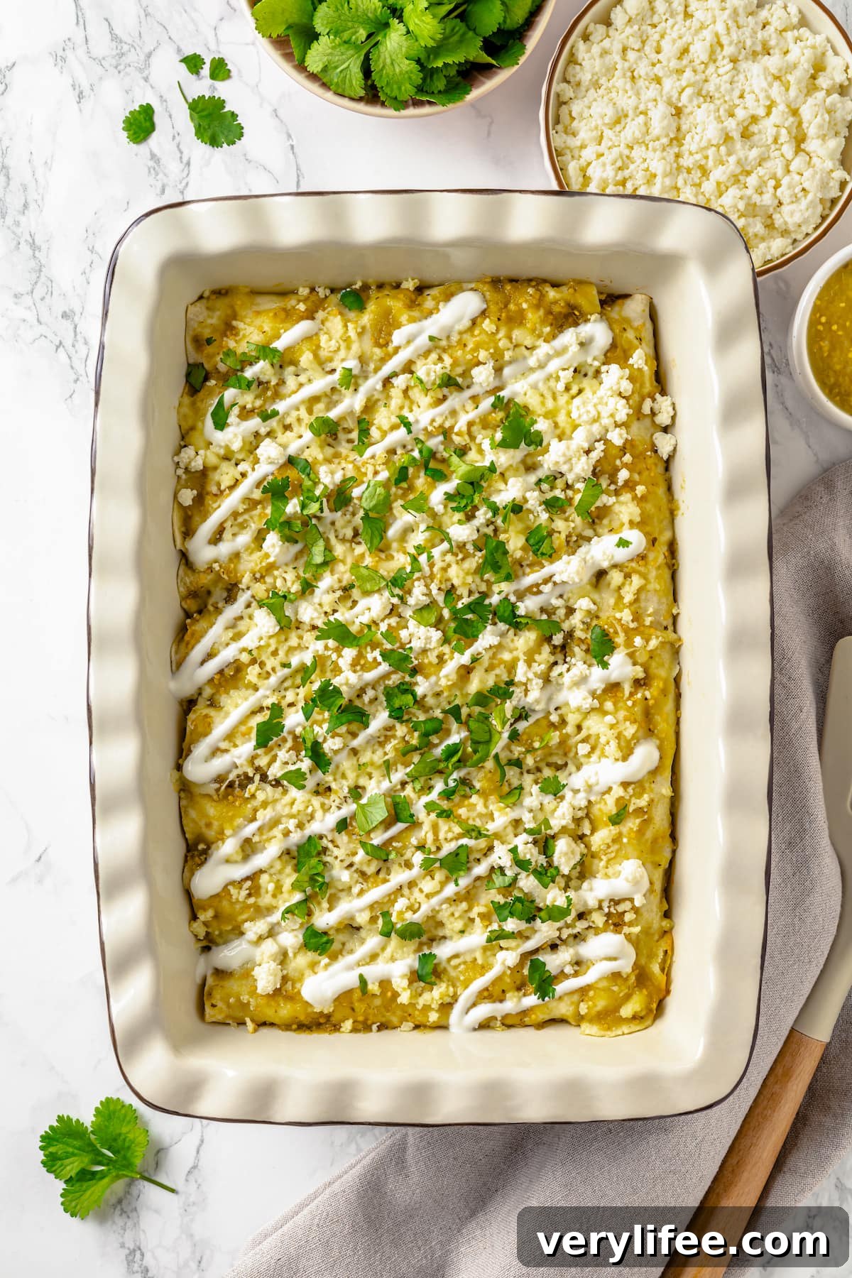 A casserole dish of enchilada verdes topped with sour cream and cilantro