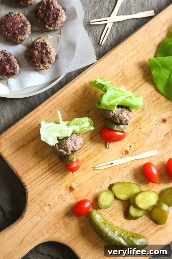 Mini Burger Skewers Recipe for Party Appetizers 2 Mini burgers with bacon, layered on a bamboo skewer with lettuce, tomatoes and pickles.