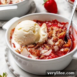 Scoop of vanilla ice cream on top of strawberry crisp in bowl