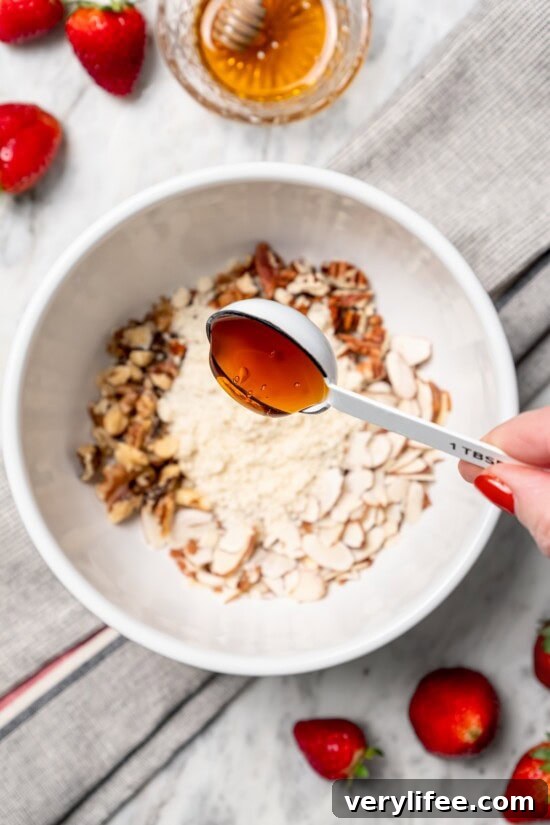 Homemade Strawberry Crisp Recipe with Oat Streusel 7 Drizzling honey from tablespoon into bowl of nuts and almond flour